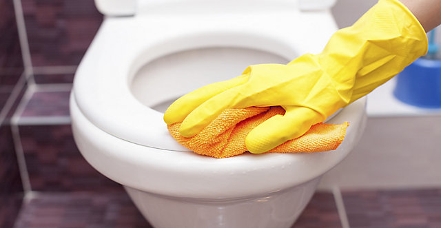 Toilet seat being cleaned with yellow rubber gloves