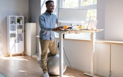 man working at a desk by a window kneeling on an exercise ball