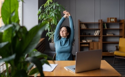 Woman stretching at a desk by a laptop
