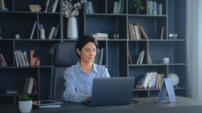 Business executive works on a laptop in a modern manager's office with bookcases behind
