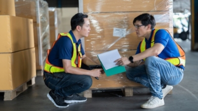 Warehouse workers check pallet wrapping to ensure cartons are bundled securely and tightly together