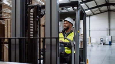 Warehouse worker operates a forklift wearing a safety hat and hi-vis jacket