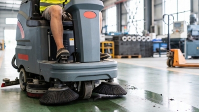 Warehouse worker in a hi-vis vest rides a floor-cleaning machine