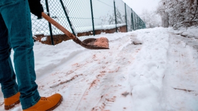 Shovelling winter grit salt onto a snowy and icy pathway
