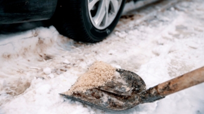 Shovelling winter grit salt onto a snowy and icy driveway